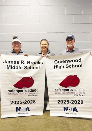 Greenwood ISD athletic trainers Sam Flores, Kim Hagelstein and Brad Brown hold up banners after the James R. Brooks Middle School and Greenwood High School athletic training programs recently received the National Athletic Trainers’ Association Safe Sports School Award for 2025–2028.