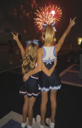 Youth cheerleaders Kynzli and Brantlee pose with their “guns up” during the fireworks show at Sunday’s homecoming tailgate.