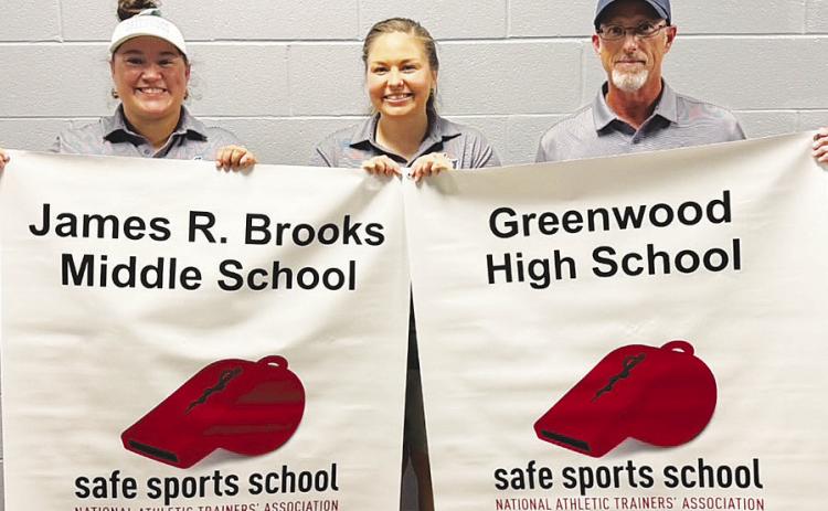 Greenwood ISD athletic trainers Sam Flores, Kim Hagelstein and Brad Brown hold up banners after the James R. Brooks Middle School and Greenwood High School athletic training programs recently received the National Athletic Trainers’ Association Safe Sports School Award for 2025–2028.